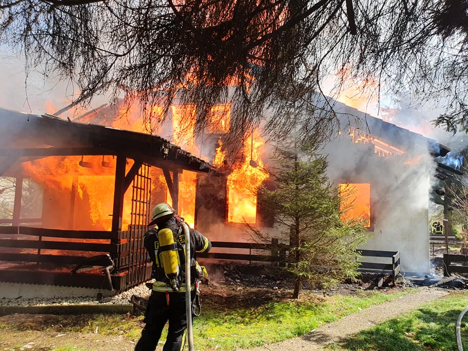 Feuerwehrmann mit Atemschutzgerät beim Löschen. Im Hintergrund Haus im Vollbrand